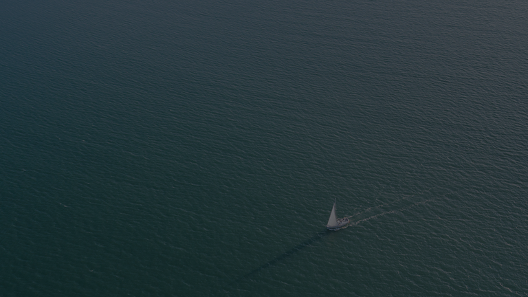 Barco à vela navega sozinho, tranquilamente, pelas águas de uma represa